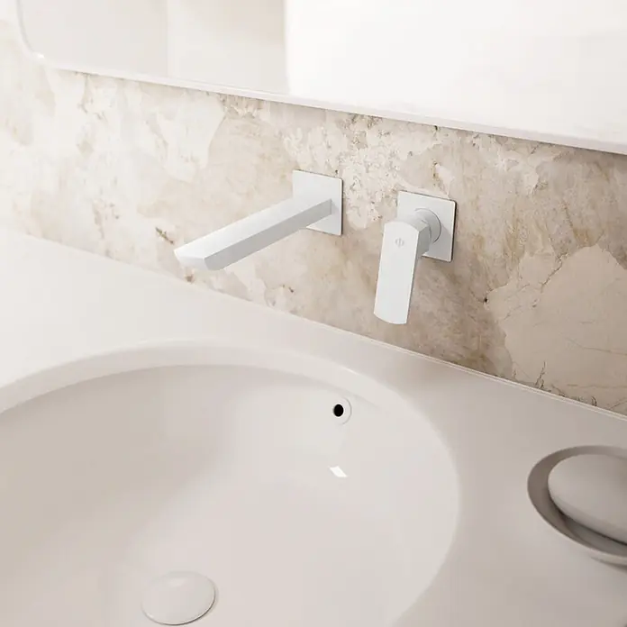 IO Grifo de lavabo empotrado Marriot - Blanco - Grifo blanco mural con caño y maneta separados, instalado sobre un lavabo blanco con un salpicadero de mármol claro.