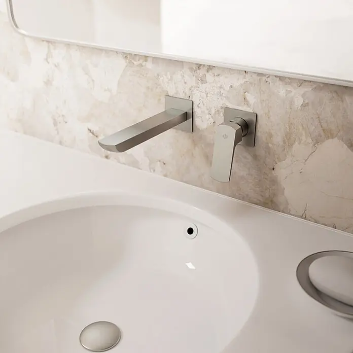 IO Grifo de lavabo empotrado Marriot - Nickel - Grifo y maneta murales de plata mate sobre un lavabo blanco, en una pared de mármol.