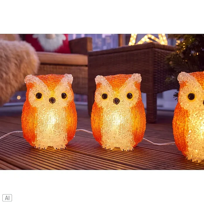 Konstsmide LED-Dekofigur Sova - Außen, Lichtfarbe: Warmweiß, Anzahl Leuchtmittel: 40 Stk., Netzbetrieben - Drei leuchtende orange-transparente Eulen-LED-Dekorationen auf einem Holzdeck, die eine warme, festliche Atmosphäre schaffen.