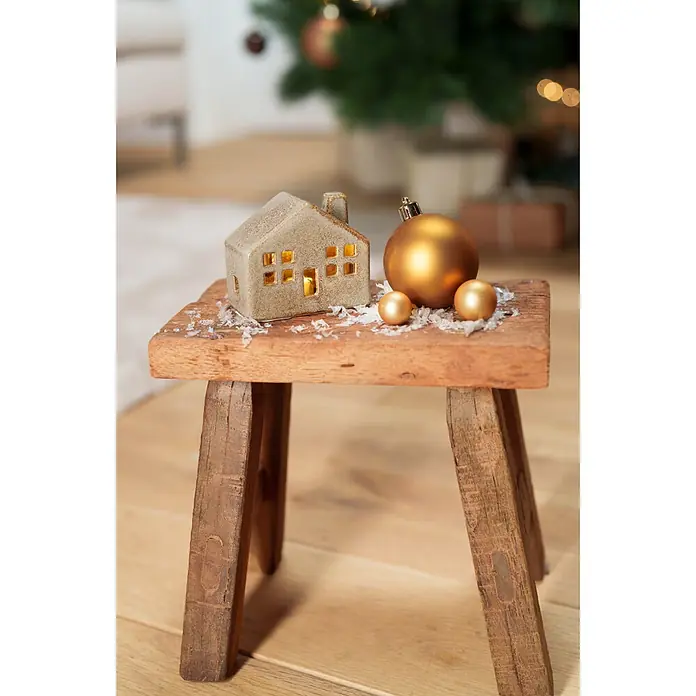 Dekoartikel LED Haus - 1 Stk., Sortiert, 8 x 4,5 x 7 cm - Kleine hellgraue Keramikhaus-Dekoration mit leuchtenden Fenstern und goldenen Kugeln auf einem rustikalen Holzschemel, für festliche Stimmung.