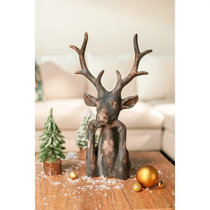 Dekofigur Hirsch Zen - L x B x H: 15 x 25,5 x 41 cm, Kunststoff, Hirsch - Dunkle Bronze-Hirschfigur mit Geweih, nachdenklich sitzend zwischen verschneiten Mini-Bäumen und goldenen Kugeln auf Holztisch für Weihnachtsdeko.