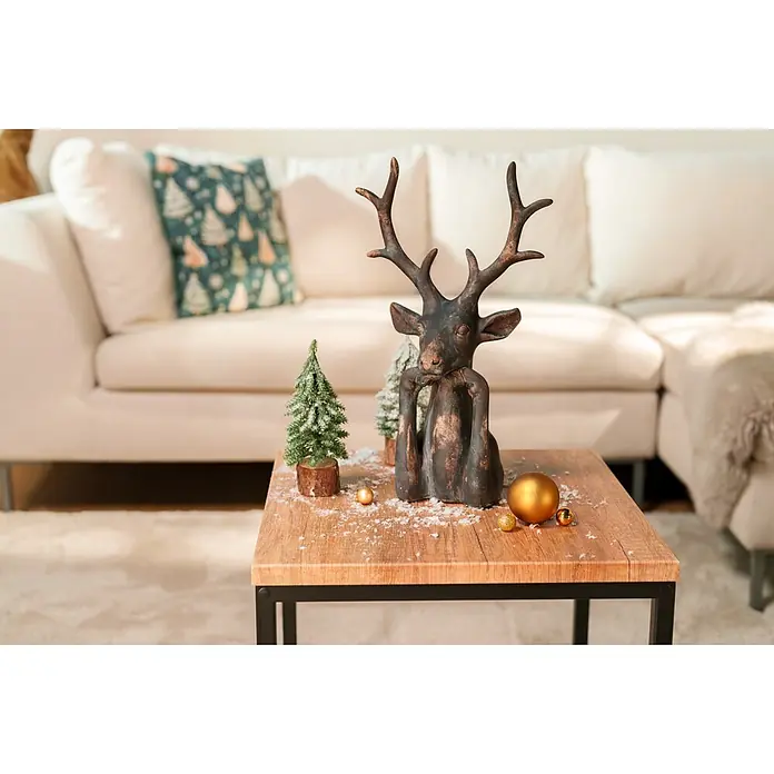 Dekofigur Hirsch Zen - L x B x H: 15 x 25,5 x 41 cm, Kunststoff, Hirsch - Eine dunkle dekorative Rentierfigur mit kleinen verschneiten Weihnachtsbäumen und goldenen Kugeln auf einem Holztisch im Wohnzimmer.
