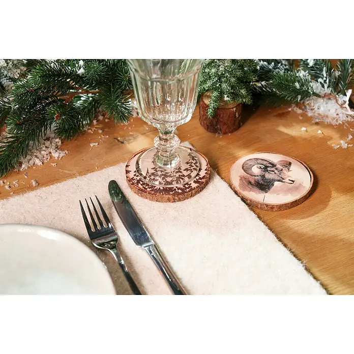 Untersetzer - 1 Stk., Sortiert, Durchmesser: 10 cm - Zwei rustikale Holzuntersetzer mit Designs und ein cremefarbener, texturierter Tischläufer auf einem gemütlichen Wintertisch.