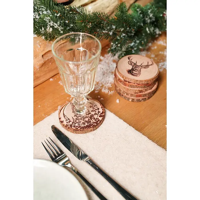 Untersetzer - 1 Stk., Sortiert, Durchmesser: 10 cm - Holzscheiben-Untersetzer mit Hirsch- und Baum-Brandmalerei-Motiven auf einem festlichen Tisch.