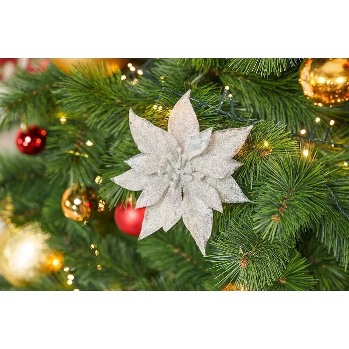 Dekoblüte Weihnachtsstern mit Clip - Durchmesser: 18 cm, Kunststoff, Silber, Christrose - Silberne Glitzer-Weihnachtsstern-Christbaumkugel, zwischen grünen Ästen und festlichen Lichtern.