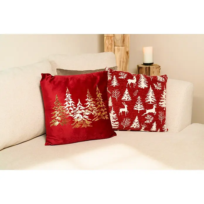 Kissen Pinegrove - 45 x 45 cm, Rot, Quadratisch - Zwei festliche rot-goldene Weihnachtskissen, eines aus Samt mit goldenen Bäumen, das andere gemustert mit weißen Bäumen und Hirschen, auf einem Sofa.