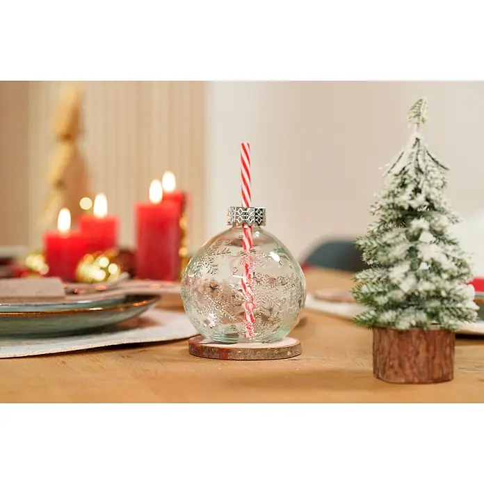 Trinkglas Partybecher Julia - Glas, Rot/Transparent - Klares Glas-Weihnachtskugel-Trinkgefäß mit Schneeflockenmuster und rot-weißem Trinkhalm auf Holzuntersetzer.