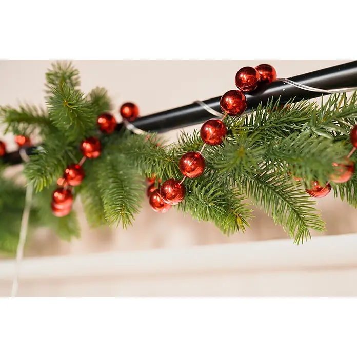 Weihnachtsgirlande Norton - Ø x L: 9 cm x 2,7 m, Kunststoff - Grüne künstliche Tannengirlande mit roten Kugeln, über einer dunklen Stange mit dezenten Lichtern drapiert.