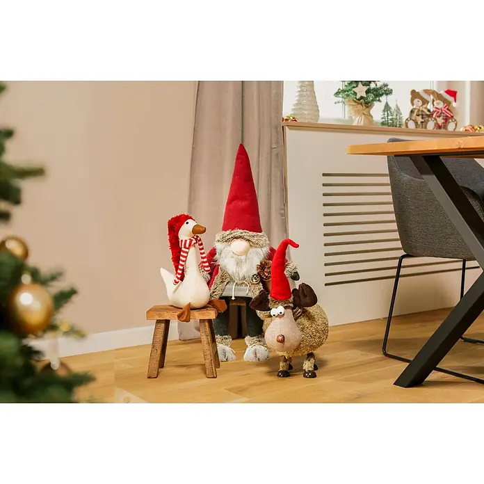 Dekofigur mit Wackeleffekt - L x B x H: 26 x 25 x 53 cm, Textil - Drei festliche Plüsch-Weihnachtsdekorationen: eine weiße Gans, ein Wichtel mit roter Mütze und ein Elch, auf Holzboden.
