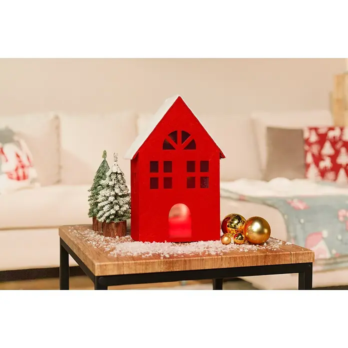Dekoartikel LED Filzhaus - 1 Stk., Sortiert, 17,5 x 8,5 x 30,5 cm - Rotes Filz-Weihnachtshaus mit verschneitem Dach, zwei kleinen beschneiten Bäumen und goldenen Kugeln auf einem verschneiten Holztisch, leuchtend von innen.