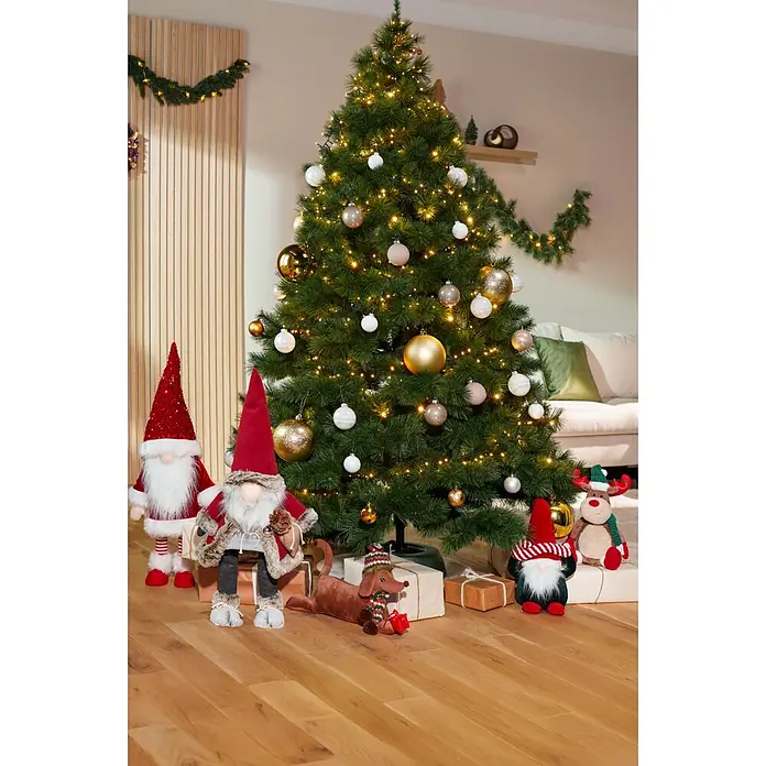 Dekofigur Weihnachtswichtel schaukelnd - L x B x H: 33 x 33 x 83 cm, Polyester - Ein hoher, grüner künstlicher Weihnachtsbaum mit warmweißen Lichtern und verschiedenen goldenen, weißen und hellbraunen Kugeln in einem festlichen Wohnzimmer.