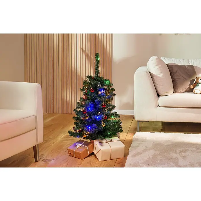 Künstlicher Weihnachtsbaum Joy - Höhe: 90 cm, Grün, LED-Beleuchtung - Kleiner künstlicher Weihnachtsbaum mit Lichtern, Kugeln und Geschenken in einem gemütlichen Wohnzimmer.