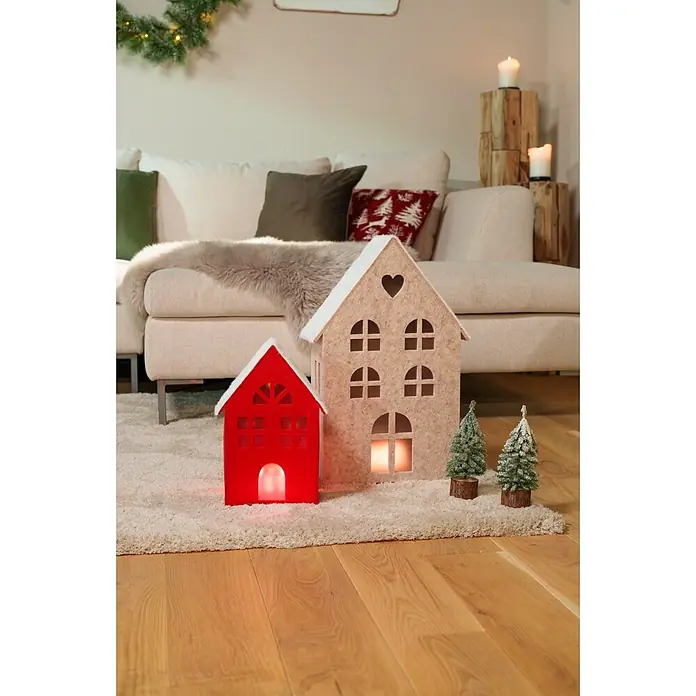 Dekoartikel LED Filzhaus - 1 Stk., Sortiert, 29 x 14,5 x 50 cm - Zwei beleuchtete Filzhäuser, rot und beige, mit kleinen verschneiten Bäumen auf einem flauschigen Teppich als festliche Dekoration.
