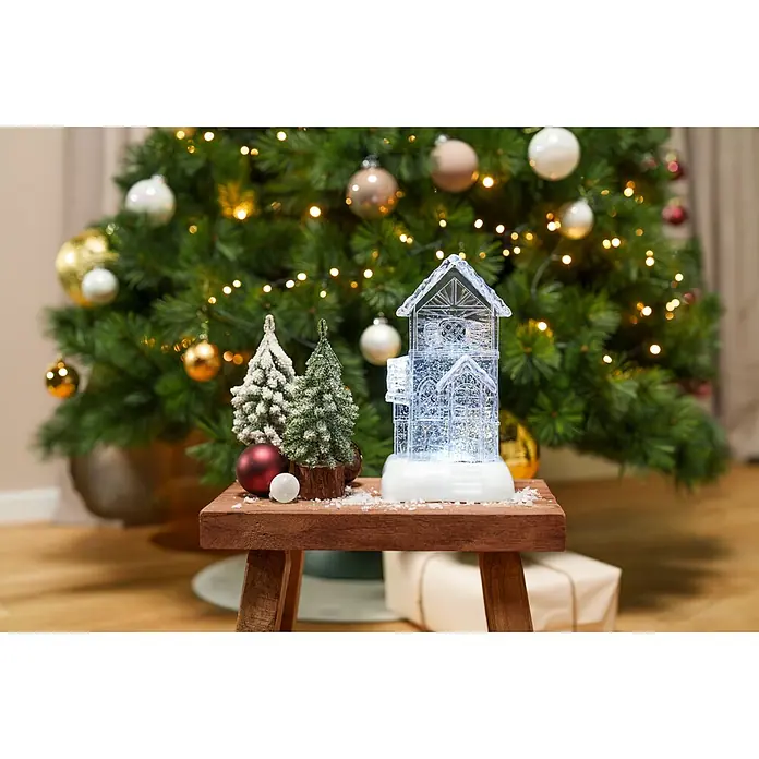 Markslöjd LED-Weihnachtsdekoleuchte Dale - 14,5 x 13 x 26 cm, Weiß/ Transparent, Batteriebetrieben, LED - Beleuchtetes Deko-Haus und verschneite Miniatur-Bäume mit Kugeln, auf einem Holzschemel präsentiert.