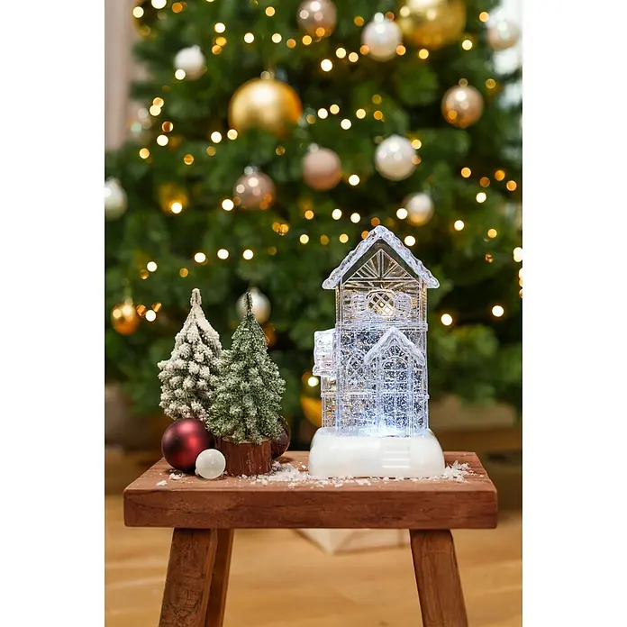 Markslöjd LED-Weihnachtsdekoleuchte Dale - 14,5 x 13 x 26 cm, Weiß/ Transparent, Batteriebetrieben, LED - Eine beleuchtete, transparente Hausdekoration mit zwei frostigen Mini-Weihnachtsbäumen und Kugeln auf einem Holzschemel, vor einem unscharfen Weihnachtsbaum.