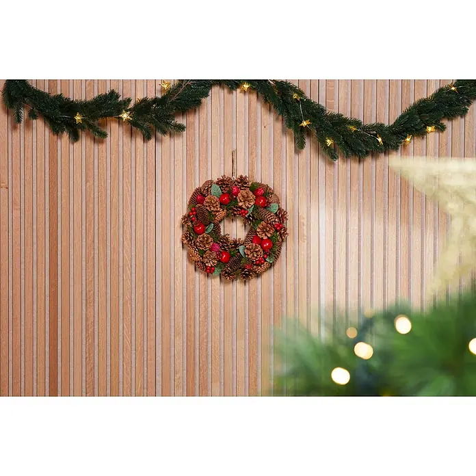 Weihnachtsgirlande Norton - Ø x L: 9 cm x 2,7 m, Kunststoff - Festlicher Weihnachtskranz aus Tannenzapfen, Beeren und Äpfeln mit Sternengirlande, an einer Holzlamellenwand.