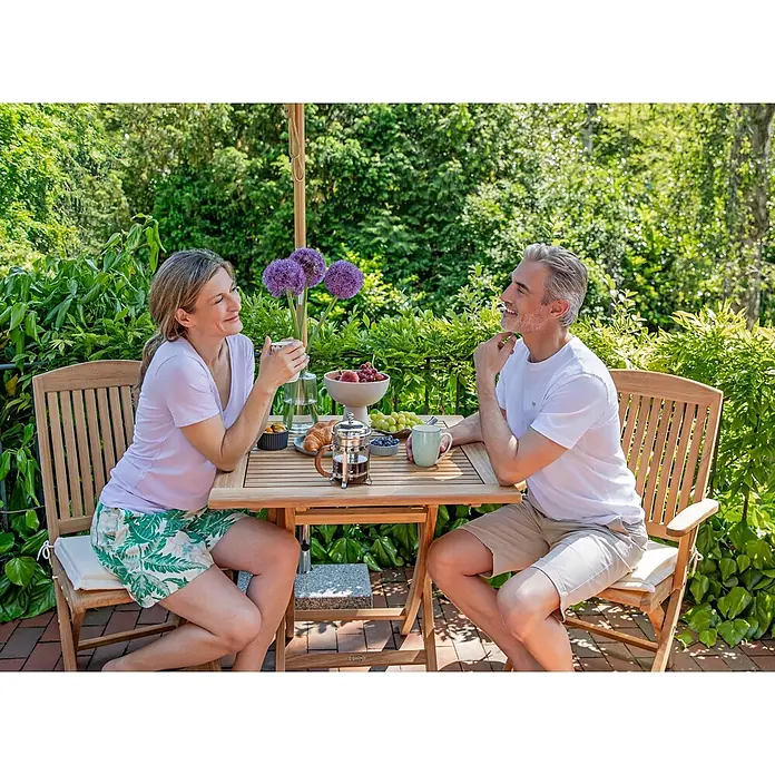 Teak Klappstuhl perfekt verarbeitet für Garten Terrasse und Balkon -  - Zwei Personen genießen ein Frühstück im Freien an einem Teakholztisch mit Stühlen im Garten.