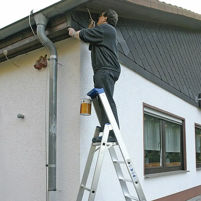 Krause Stehleiter - Arbeitshöhe: 3,4 m, Anzahl Tritte: 6 Stk., Belastbarkeit: 150 kg, Aluminium - Ein Mann, der auf einer Aluminiumleiter steht und ein Haus streicht. Die Leiter ist ein stabiles und praktisches Werkzeug für diese Arbeit.