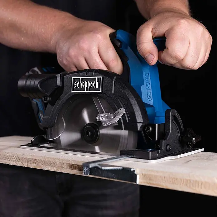 Scheppach IXES 20V Akku-Handkreissäge BC-HCS165-X - 20 V, Durchmesser Sägeblatt: 165 mm - Person schneidet ein Holzbrett mit einer blauen und schwarzen Scheppach Akku-Kreissäge, Sägeblatt in Bewegung.
