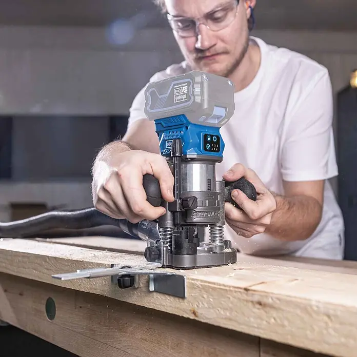 Scheppach IXES 20V Akku-Oberfräse BC-EHR24-X - 20 V, Ohne Akku, 10.000 U/min - 30.000 U/min, 8 mm - Mann bearbeitet ein Holzbrett mit einer blauen und grauen Scheppach Akku-Oberfräse.