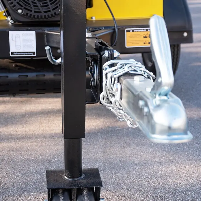 BAMATO Holzhäcksler HACK-150PRO 18kW Einzugswalze bis 150mm -  - Eine verzinkte Anhängerkupplung mit Sicherheitsketten, verbunden mit einem schwarzen Anhängerrahmen, neben einem schwarzen Stützrad auf Asphalt.