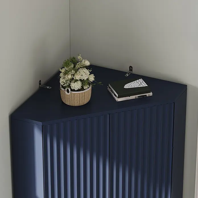 SONNENH Eckschrank mit 4 Türen und verstellbaren Böden, Blau -  - Dunkelblauer Eckschrank mit geriffelten Türen, dessen Oberfläche einen Blumenstrauß und Bücher trägt.