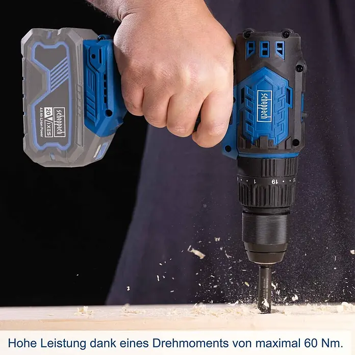 Scheppach IXES 20V Akku-Schlagbohrschrauber BC-CD60-X - 20 V, Ohne Akku, 60 Nm - Eine Hand bohrt mit einem blau-schwarzen Scheppach 20V Akku-Bohrschrauber in Holz und erzeugt Späne.