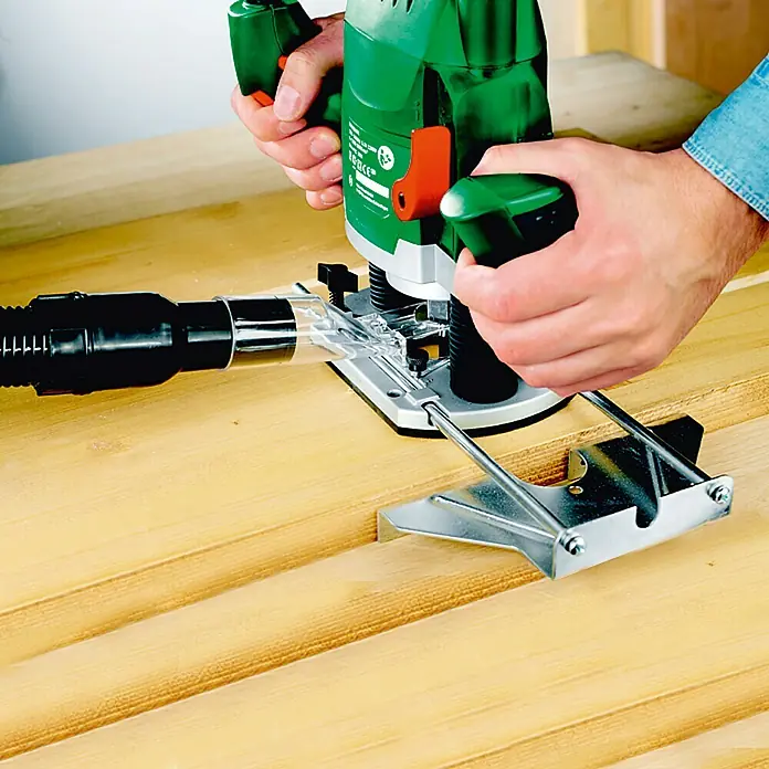 Bosch Fresadora eléctrica POF 1200 AE - 1.200 W, 11.000 r.p.m. - 28.000 r.p.m., Diámetro del portaherramientas: 6 mm - 8 mm - Una fresadora vertical Bosch verde se utiliza para cortar una ranura en una tabla de madera, con un accesorio de aspiración para la eliminación de polvo.