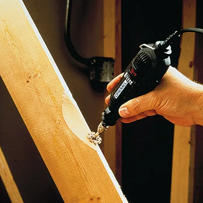 Dremel Trenn- & Formscheibe Mod. 542Arbeitsdurchmesser: 25,4 mm, Geeignet für: Holz - Nahaufnahme eines Dremel-Rotationswerkzeugs, das in der Hand gehalten wird und ein Stück Holz bearbeitet.