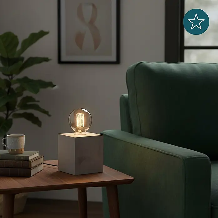 Luxula Deko-Tischleuchte Modern Minimalistisch E27 Fassung Metall Design -  - Eine Tischlampe mit Betonfuß und sichtbarer Edison-Glühbirne beleuchtet einen Holznebentisch neben einem grünen Sofa und schafft ein warmes Ambiente.