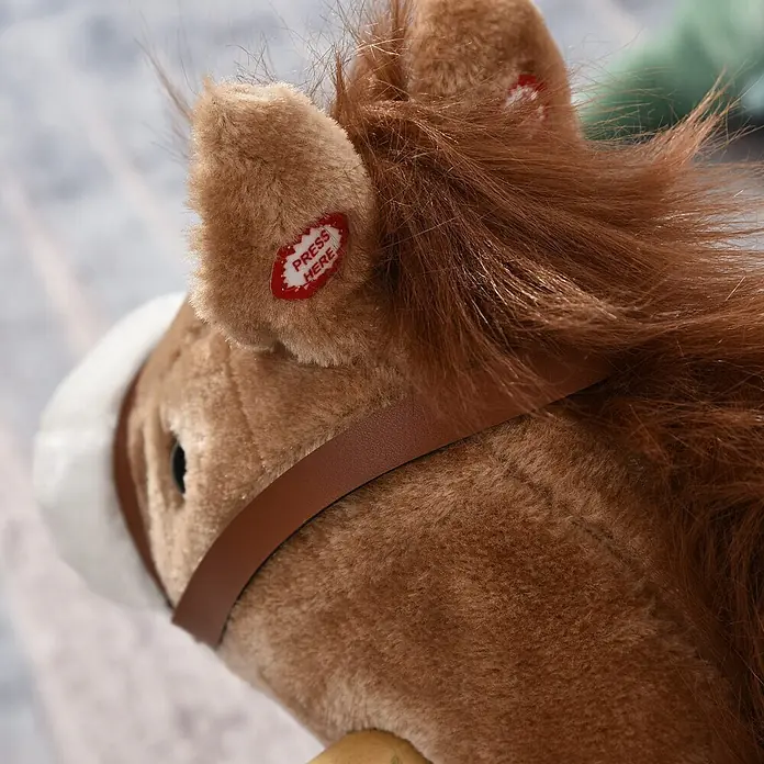 Kinder Schaukelpferd Baby Schaukeltier Pferd Spielzeug Braun -  - Nahaufnahme des Kopfes eines braunen Plüschpferdes mit Mähne, weißem Zaumzeug und braunem Riemen. Ein roter "PRESS HERE"-Knopf ist am Ohr sichtbar.