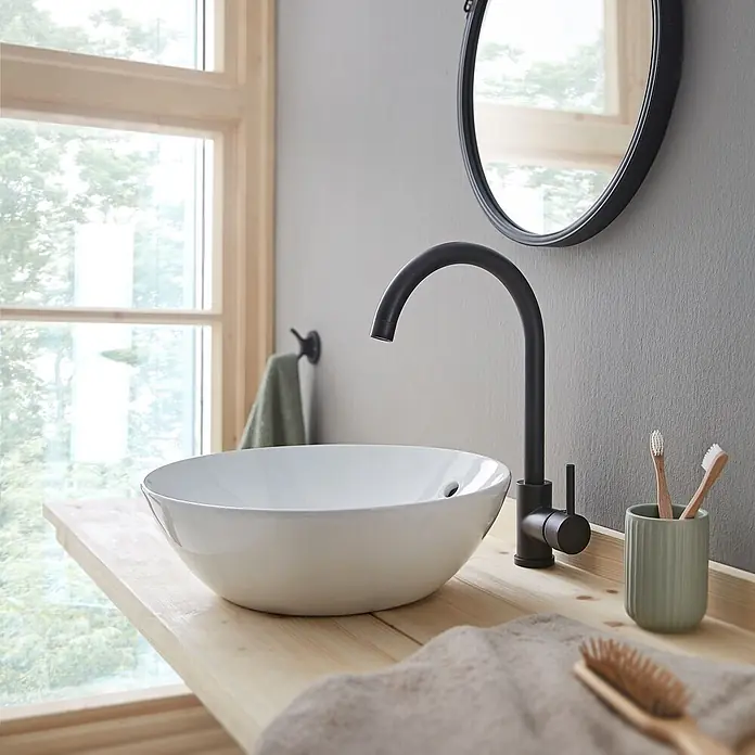 SCHÖNER WOHNEN-Kollektion Aufsatzwaschbecken Beco 38 cm Weiß - Ohne Spezialglasur, Hahnloch: Ohne, Mit Überlauf, Weiß - Ein modernes Badezimmer mit einem weißen Aufsatzwaschbecken auf einer hellen Holzplatte, ergänzt durch einen mattschwarzen Wasserhahn und runden Spiegel.