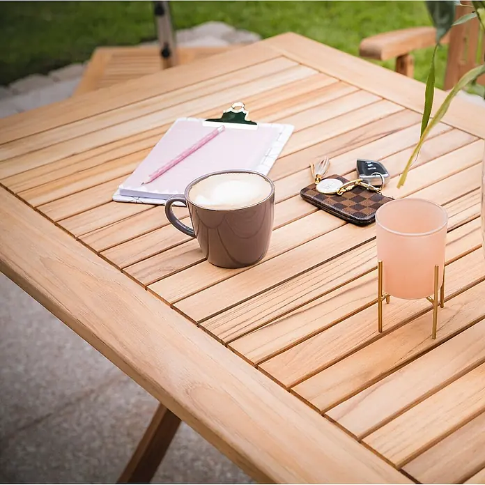 Klapptisch Fano Camping Teak Holz Tisch 120 x 70 cm Balkontisch Massivholz -  - Quadratischer Gartentisch aus Holzlatten mit Kaffeetasse, Notizbuch, Schlüsseln und rosa Kerzenhalter.
