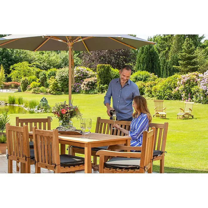 Kai Wiechmann Gartentisch - Teakholz, Rechteckig, Naturbelassen - Hölzernes Outdoor-Essgruppe mit Kissen, genutzt von einem Paar beim Getränke genießen.