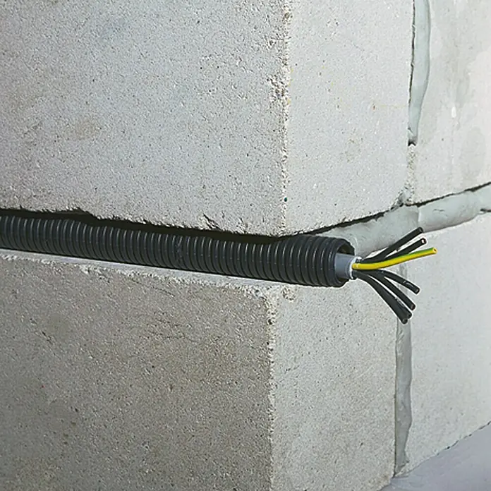 Gewiss Flexrohr - 25 m, Kunststoff, 750 N, Schwarz, 50 mm - Ein flexibles, gewelltes Elektroinstallationsrohr mit Kabeln, das zwischen Betonblöcken verläuft und elektrische Leitungen schützt.
