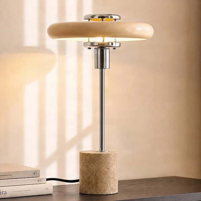 Lindby Tischlampe in beige, Nachttischlampe -  - Moderne Tischleuchte mit beigem Schirm, Chromfuß und zylindrischem Steinsockel, die warmes Licht auf einen Holztisch wirft.