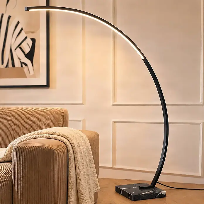 Lindby LED Stehlampe in schwarz, Bogenlampe Wohnzimmer -  - Moderne Bogenstehlampe mit schwarzem Metallgestell und LED-Licht, Marmorsockel, beleuchtet Wohnzimmer neben Sessel.