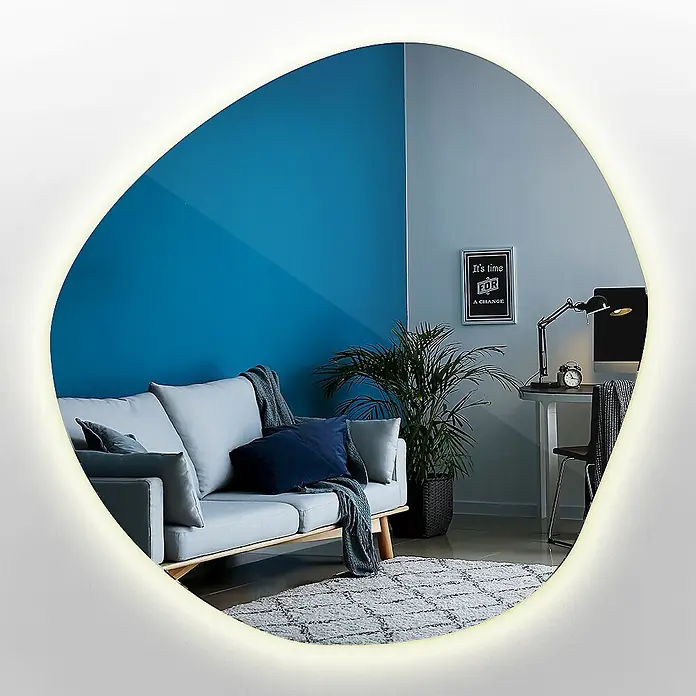 Tulup Wandspiegel -  - Unregelmäßig geformter, beleuchteter Spiegel, der einen modernen Wohnraum mit blauer Wand und Sofa reflektiert.