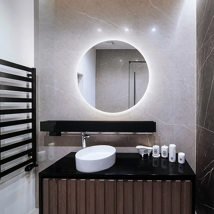 Tulup Wandspiegel -  - Modernes Badezimmer mit Holzwaschtisch, schwarzer Arbeitsplatte, weißem Waschbecken, hinterleuchtetem Spiegel und schwarzem Handtuchwärmer.