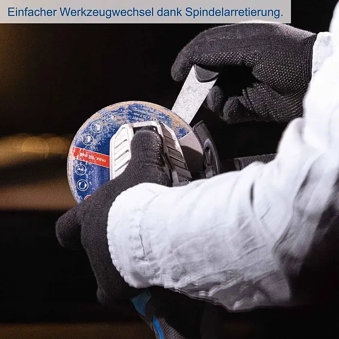 Scheppach IXES 20V Akku-Winkelschleifer C-AG125-X - Ohne Akku, Durchmesser Scheibe: 125 mm - Behandschuhte Hände wechseln eine Trennscheibe an einem Winkelschleifer mit einem Schlüssel, was einen einfachen Werkzeugwechsel zeigt.