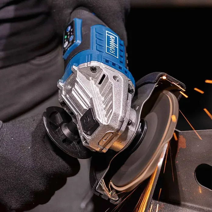 Scheppach IXES 20V Akku-Winkelschleifer BC-AG125-X - 20 V, Ohne Akku, Durchmesser Scheibe: 125 mm - Eine Person in schwarzen Handschuhen benutzt einen blau-silbernen Scheppach Winkelschleifer zum Trennen von Metall, wobei Funken fliegen.