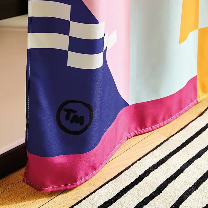 Tohaa Design Duschvorhang BonBon Balm - Tierney Milne -  - Farbenfroher Vorhang mit Schachbrettmuster, abstrakten Formen und 'TM'-Symbol, auf Holzboden neben gestreiftem Teppich.