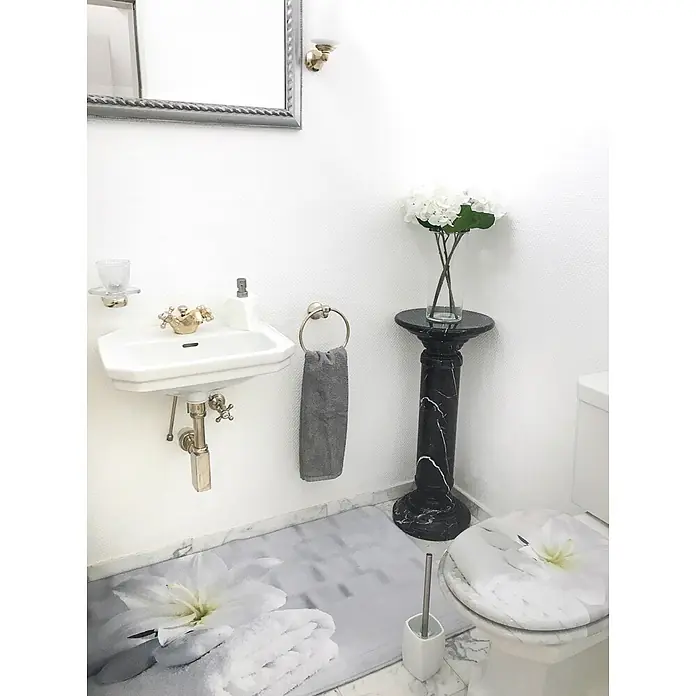 SANILO Badteppich Good Feeling 70 x 110 cm - 70 x 110 cm, Polyester, Weiß - Kleines, elegantes Badezimmer mit weißem Waschbecken, Toilette mit Blumenmotivdeckel, schwarzem Marmorsockel mit weißen Blumen und gemusterter Bodenmatte.