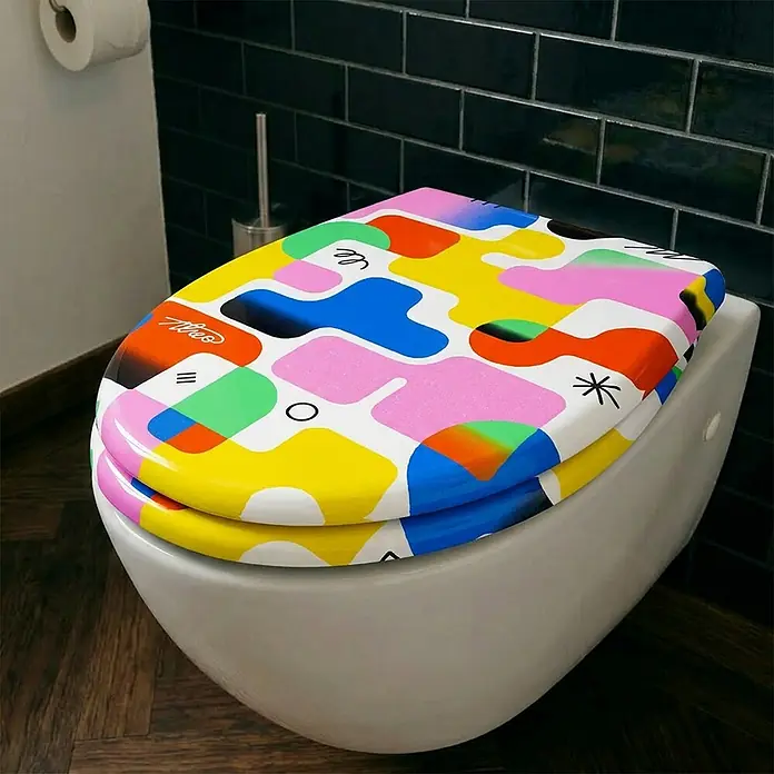 Wodea WC-Sitz   -  Colors -  - Eine Toilette mit einem bunten, abstrakt gemusterten Toilettensitz in Gelb-, Pink-, Blau- und Grüntönen, der dem Badezimmer einen lebendigen Akzent verleiht.