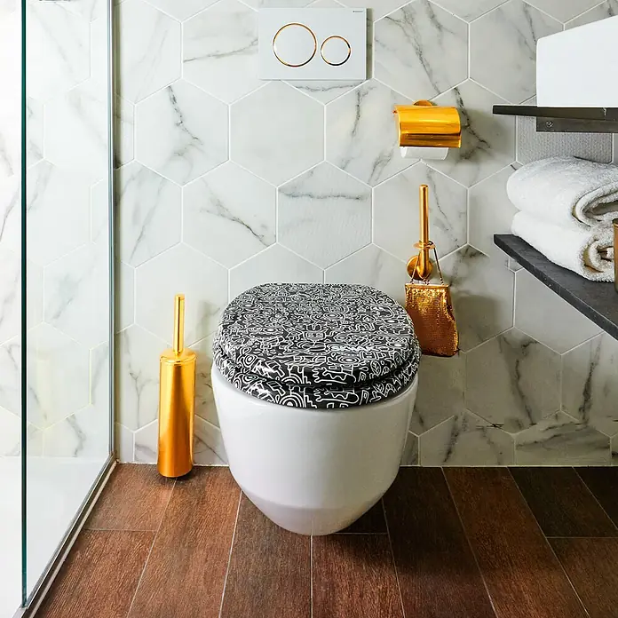 TohaaDesign WC-Sitz Cyborg - Skwak -  - Weißes WC mit schwarz-weiß gemusterter Sitzfläche in einem modernen Bad, ergänzt durch goldene Accessoires.