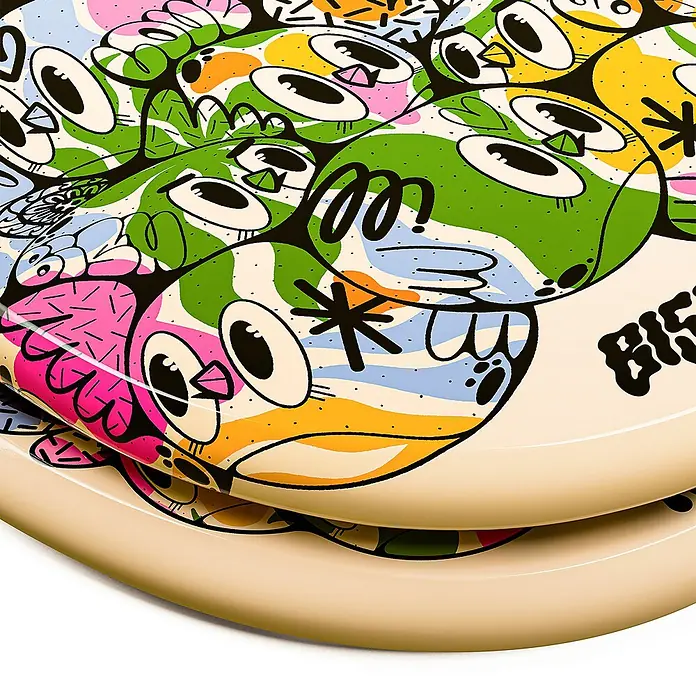 Tohaa Design WC-Sitz Color Bomb - Bishop Parigo -  - Gestapelte beigefarbene Teller mit lebhaften, cartoonartigen Vogelillustrationen in verschiedenen Farben, mit kräftigen schwarzen Konturen.