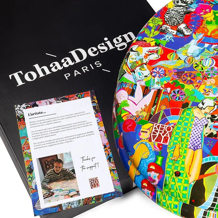 TohaaDesign WC-Sitz Grave - Guive Khosravi -  - Ein farbenfrohes Pop-Art Keramikobjekt neben seiner schwarzen TohaaDesign Box und einer Künstlerkarte.