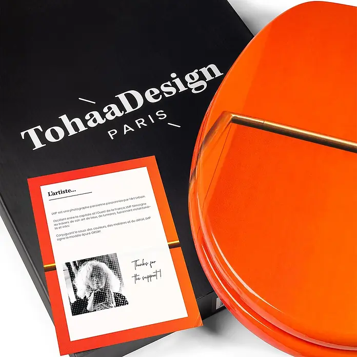 Tohaa Design WC-Sitz Orsay - LMP -  - Glänzendes, leuchtend orangefarbenes Designobjekt, vielleicht Tablett oder Deckel, mit goldenem Akzentstab, auf Markenverpackung.
