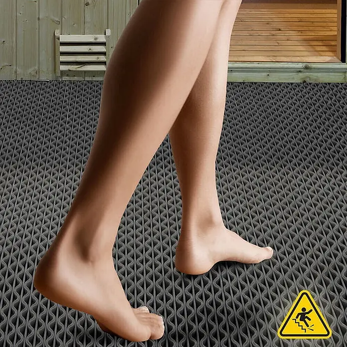 Floordirekt Antirutschmatte Anti-Slip für Barfußzonen - UV-beständig - Grau - 90 x 50 cm - Grau - Barfuß gehen auf einer grauen, strukturierten Antirutschmatte mit Wellenmuster und gelbem Rutschgefahr-Warnschild, vor einem Saunaeingang.