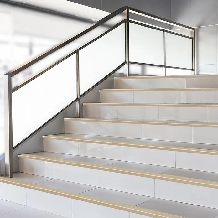 Floordirekt Stufenkantenprofil Safety F-Form Gold 100x5,3 cm Vorgebohrt -  - Beige Antirutschstreifen auf weiß gefliesten Treppen mit Metall- und Milchglasgeländer.